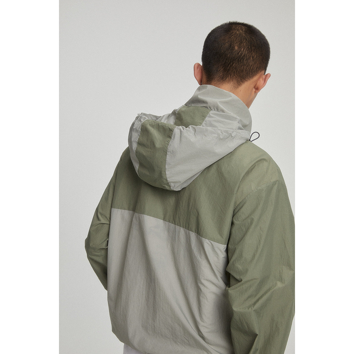 Close rear view of an olive green and light gray color-block jacket with a large hood.