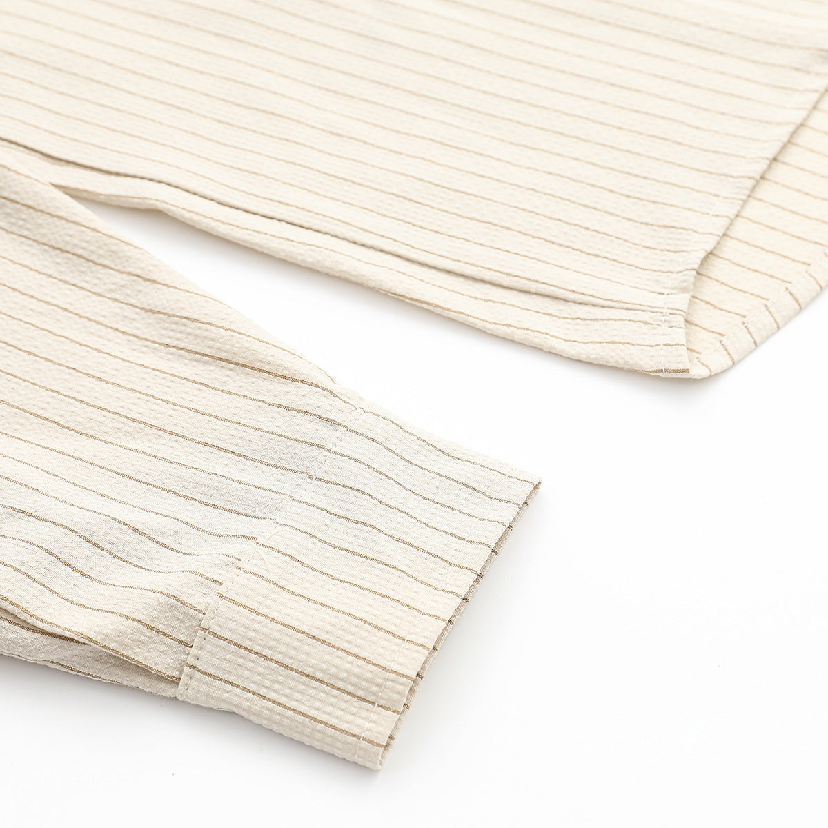 Close-up of the ivory shirt’s striped fabric and stitched sleeve cuff and hem edges.