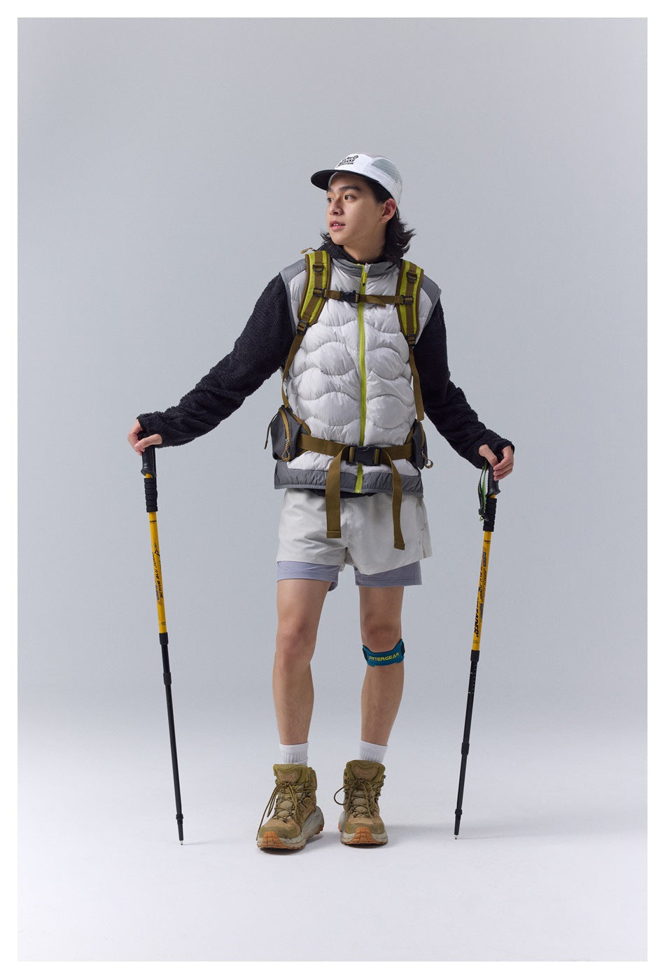Front view of a hiker wearing a white quilted vest with lime zipper trim, dark fleece sleeves and hiking gear.