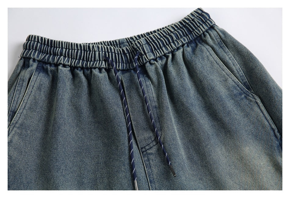 Close-up of the elastic waistband, navy drawstrings, and front pocket area of blue-gray denim shorts.