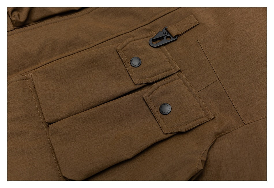 Close-up of brown coat pocket flaps with dark buttons and a black clip attached to a fabric loop.