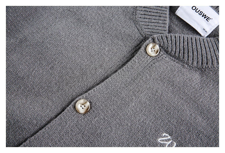 Close-up of a charcoal gray cardigan’s knit texture, two cream buttons, and a small embroidered chest motif.