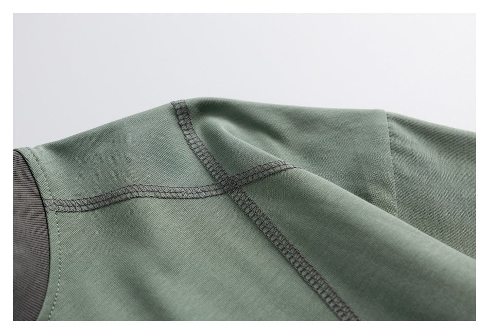 Close-up of a sage-green garment showing shoulder seams and dark overlock stitching.