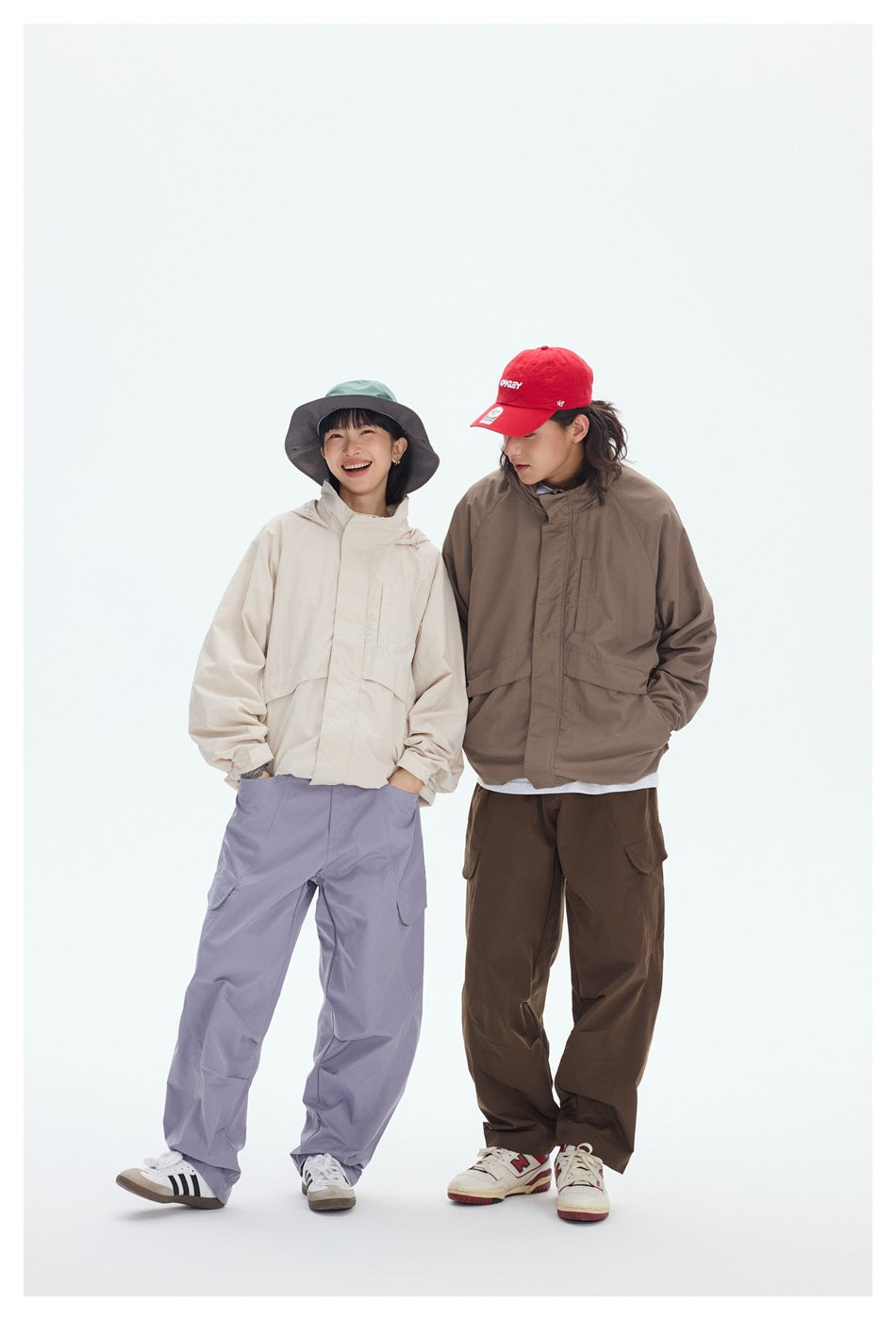 Two models pose in cream and taupe hooded jackets with loose cargo pants and hats.