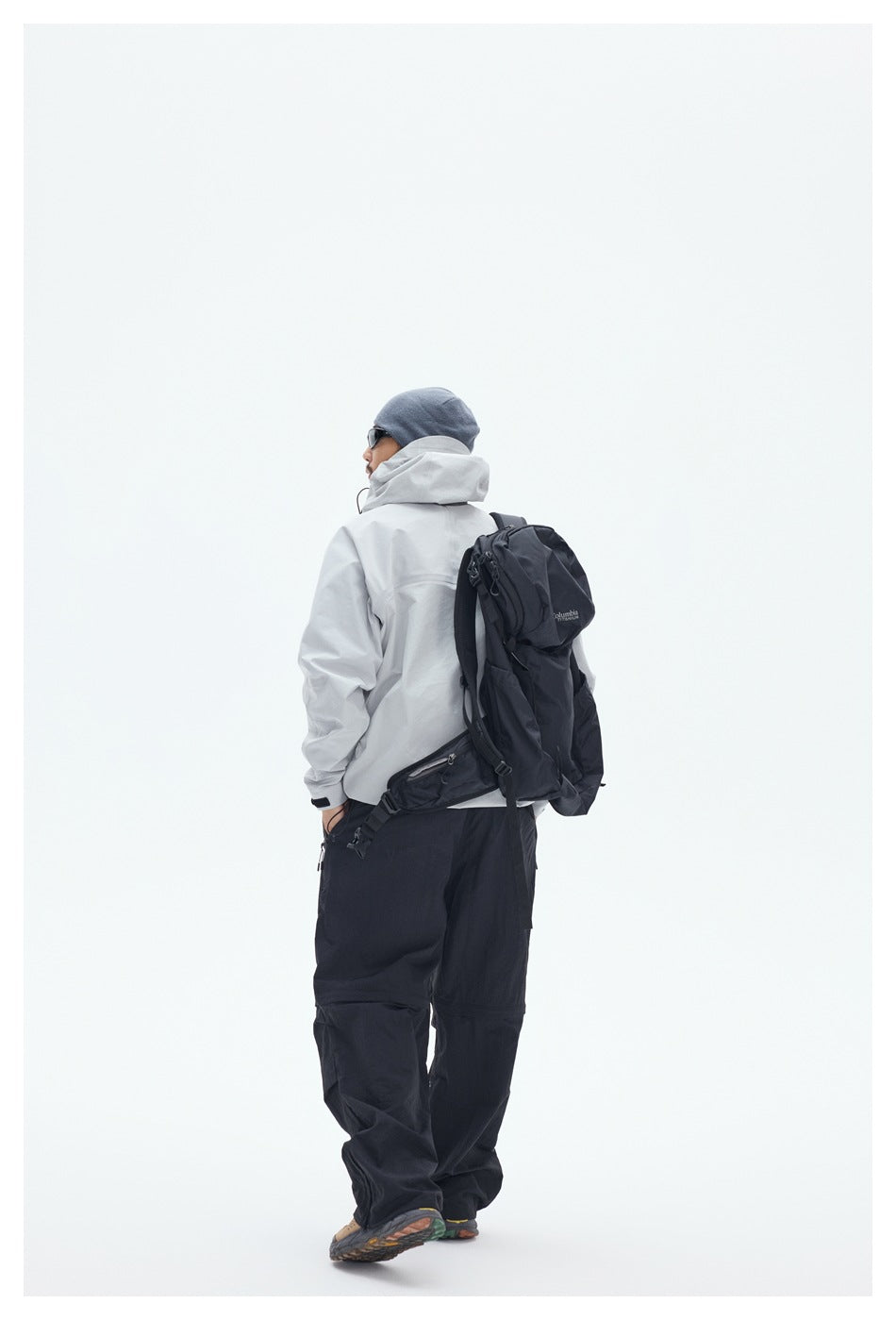 Rear view of a man wearing a light gray hooded jacket, black pants, and a black backpack.