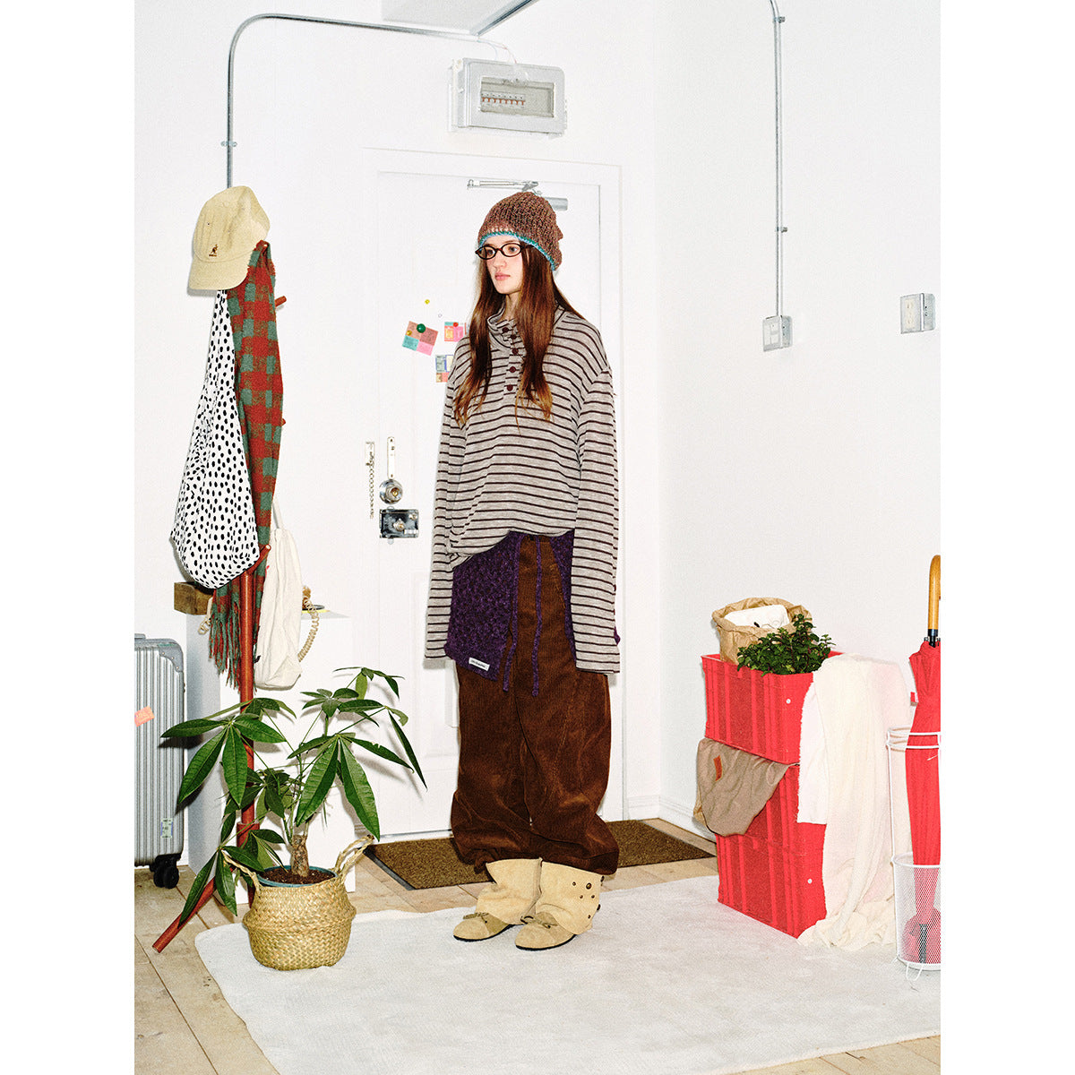 Front view of a model in an oversized gray-and-black striped henley, brown trousers, and a purple knit wrap.
