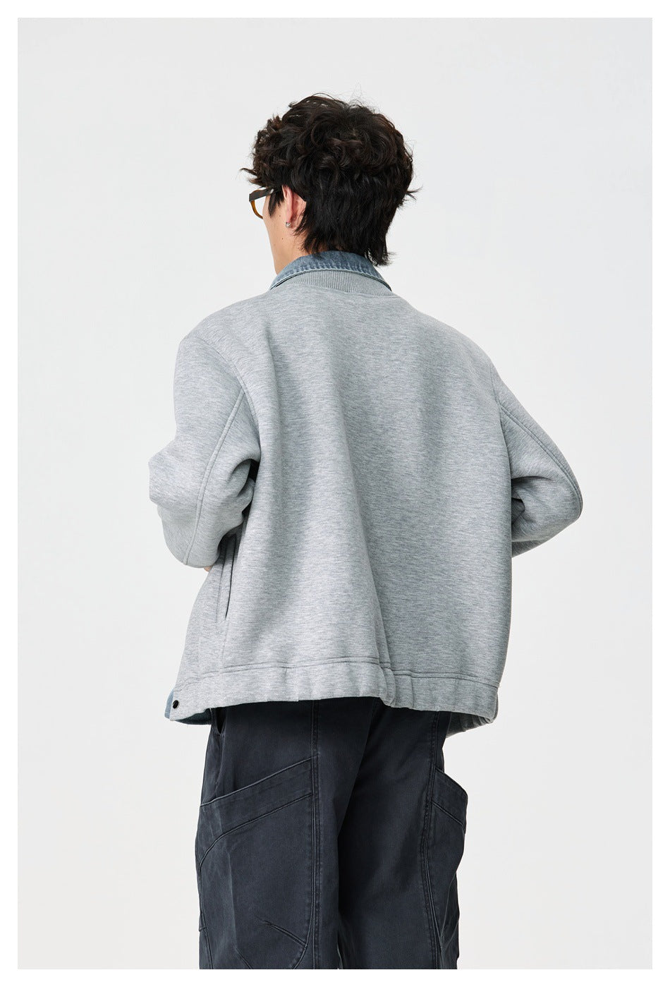 Closer back view of a model wearing a light gray jacket with a blue denim collar and dark cargo pants.