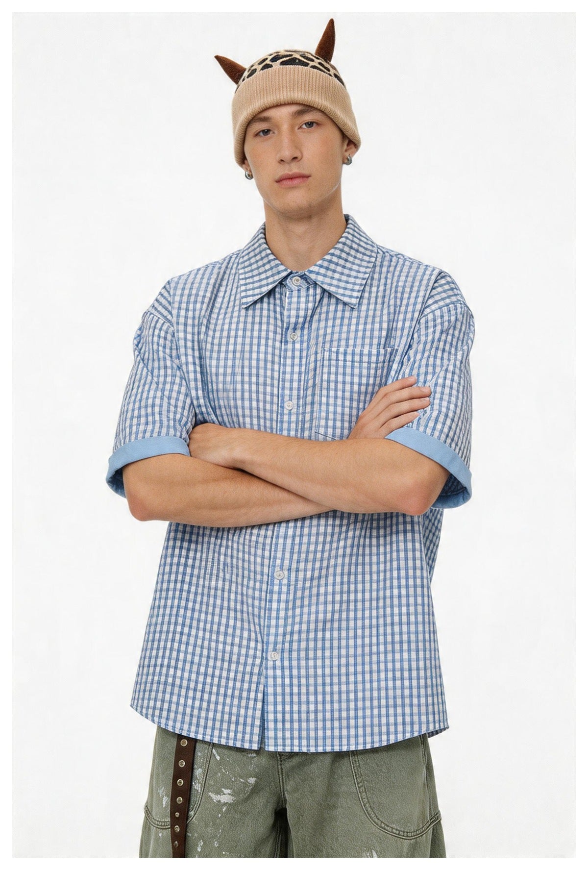 Model wearing a blue and white check short-sleeve button-up shirt with arms crossed, paired with green pants
