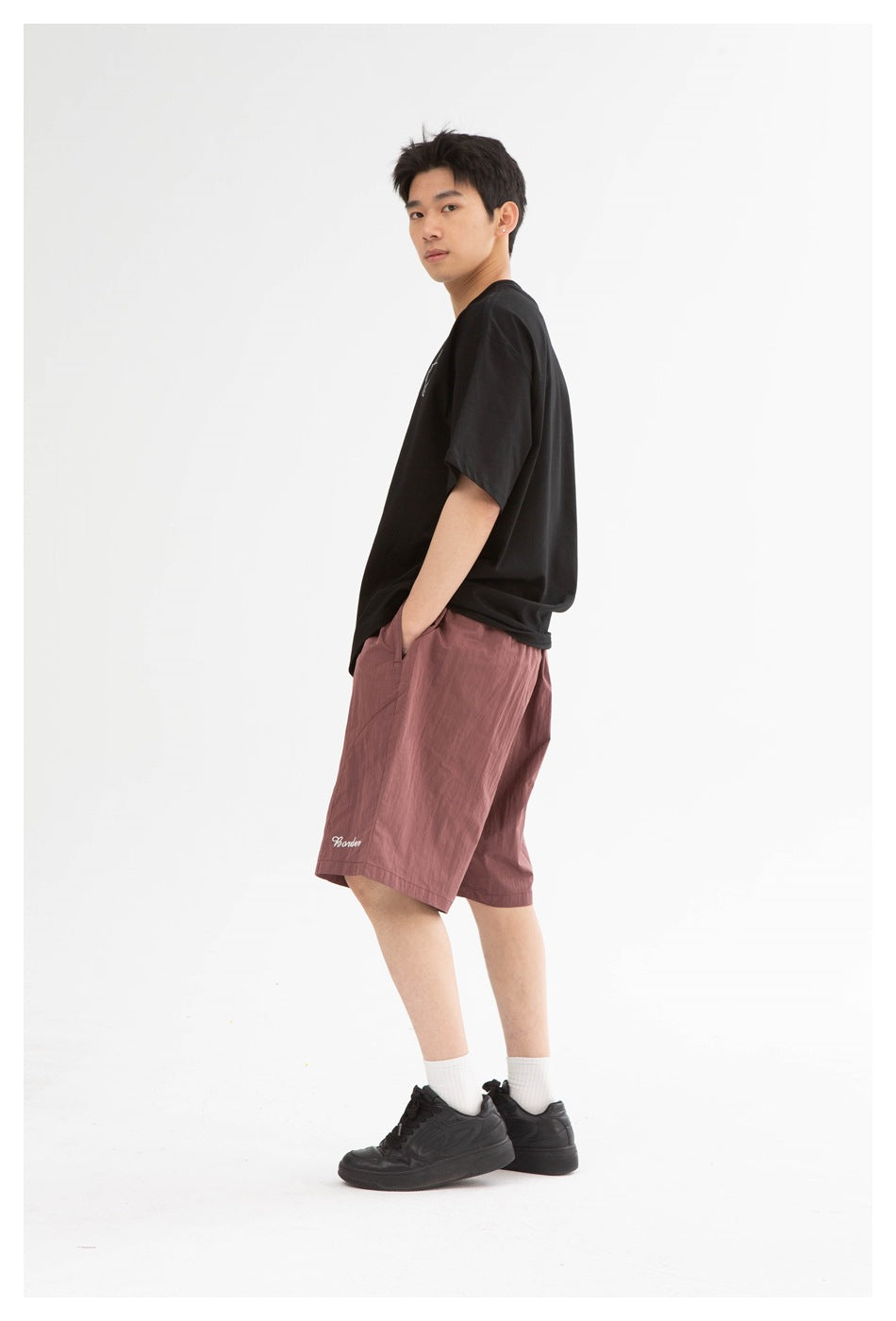 Model wearing mauve knee-length shorts with a black T-shirt, white socks, and black sneakers.