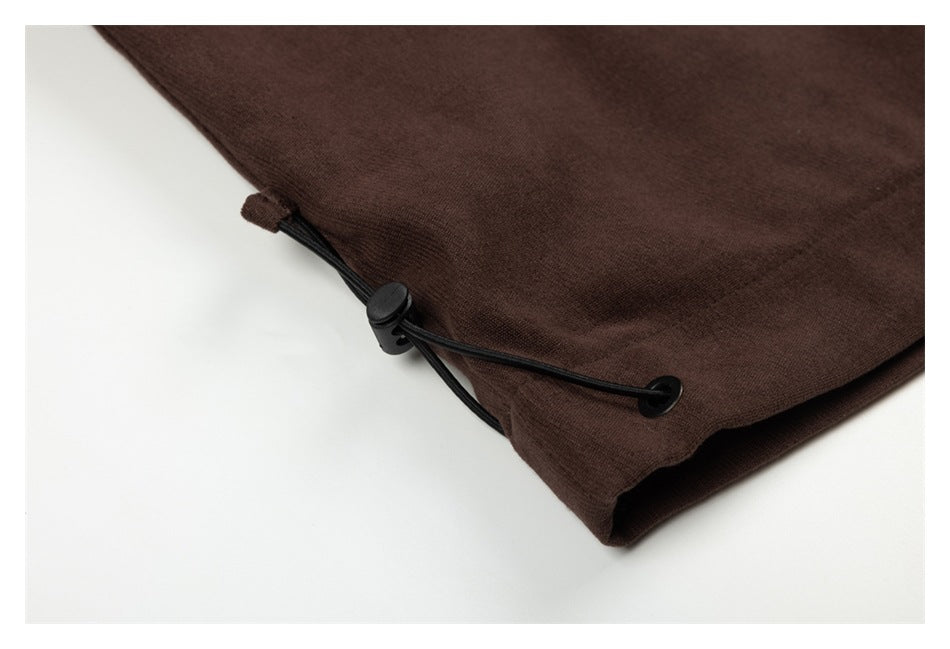 Close-up of dark brown garment fabric with a black drawcord, toggle, and eyelet.