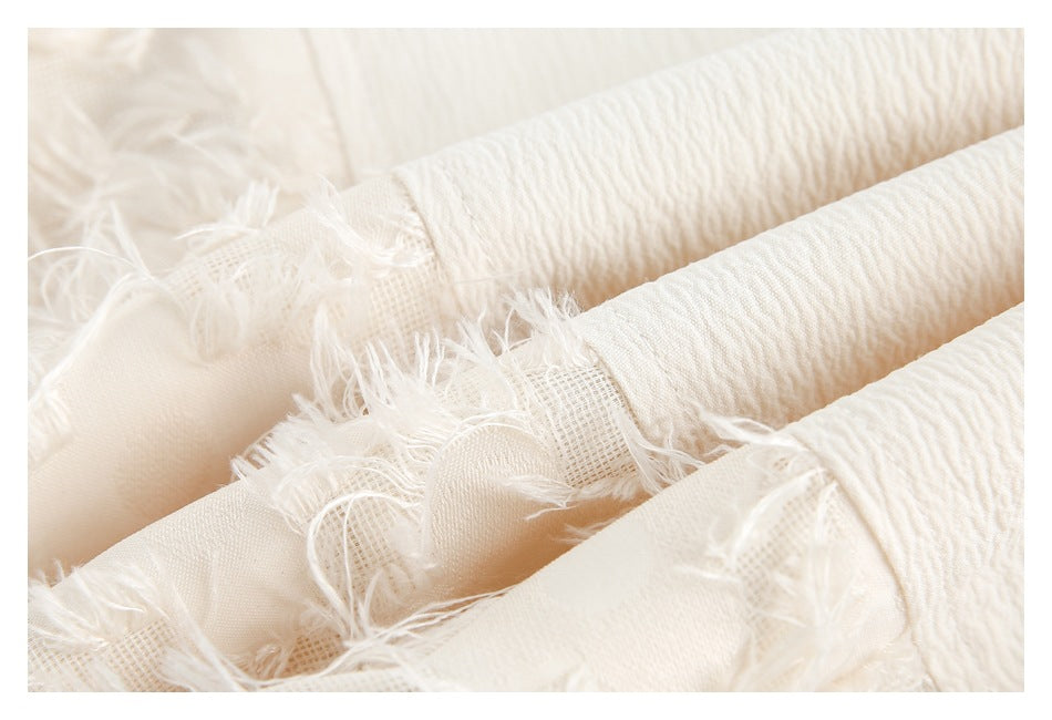 Close-up of ivory textured fabric with gathered folds, mesh sections, and frayed edges.