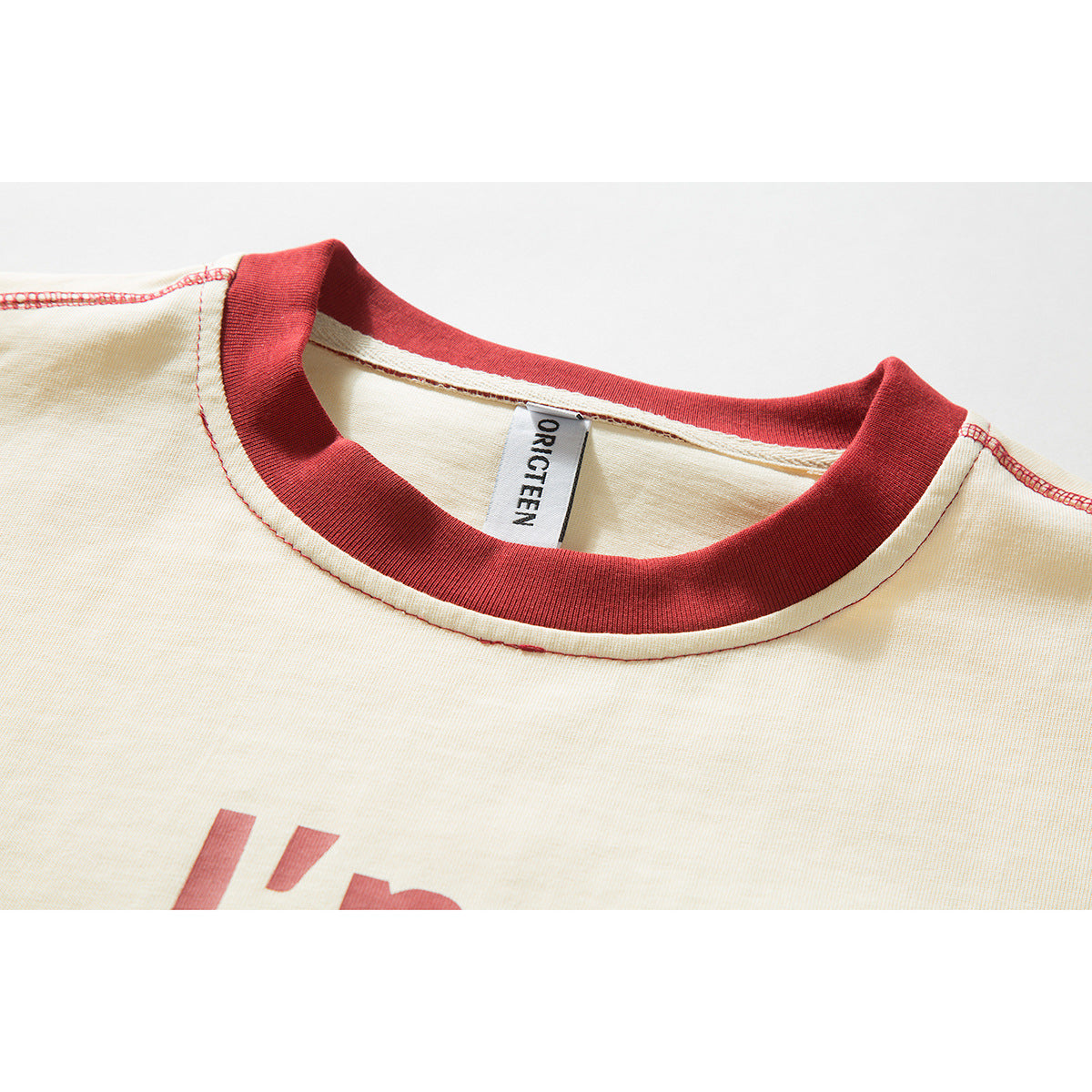 Close-up of an ivory T-shirt with a dark red ribbed crew neck, red stitching, and a sewn-in neck label.