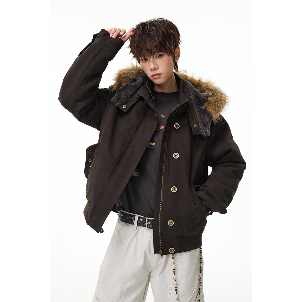 Model wearing a dark brown hooded jacket with tan fur trim and brass-tone buttons over a black shirt.