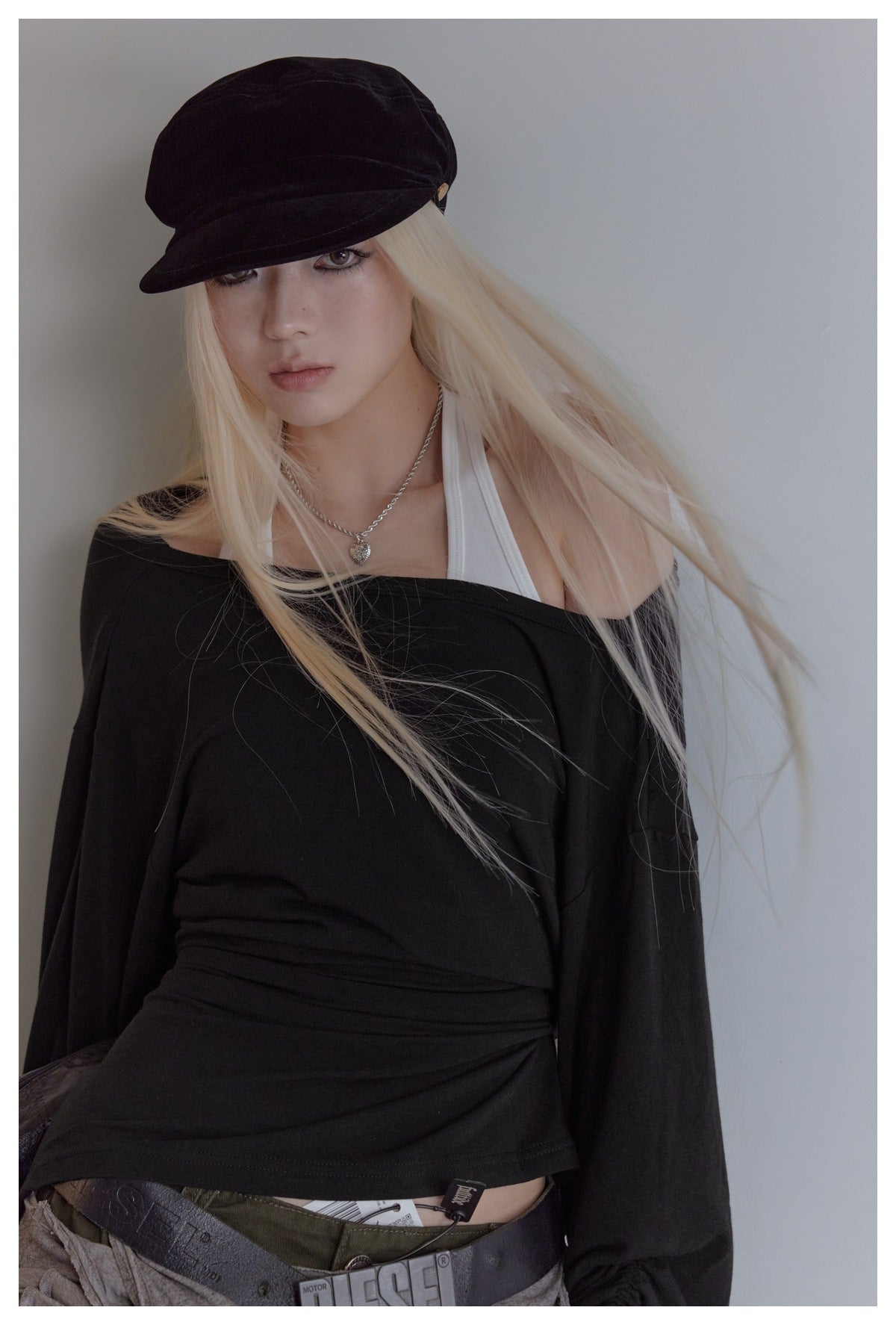 Close view of a model wearing a black off-shoulder top over a white halter top and a black cap.