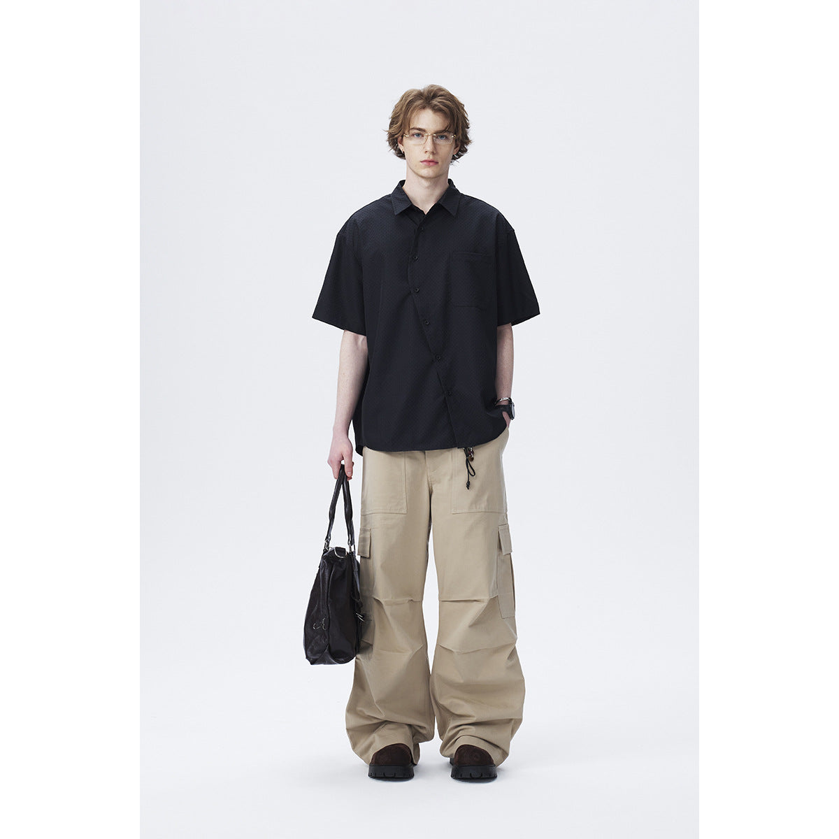 Model wearing a black short-sleeve button-up shirt with a chest pocket and loose beige cargo trousers.