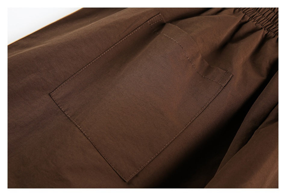 Close-up of a large stitched pocket on dark brown pants, with part of the elastic waistband visible.