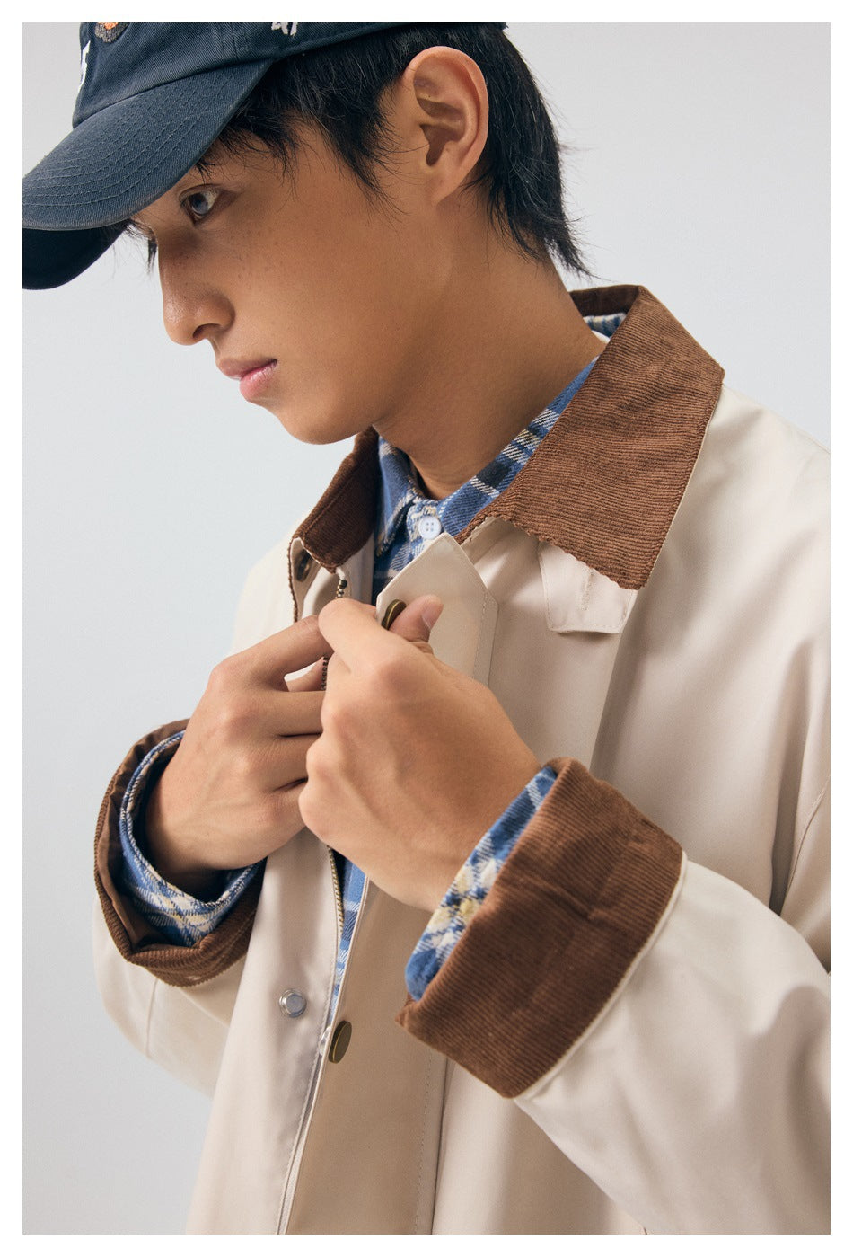 Close-up of the beige coat's brown corduroy collar and cuffs, snap fasteners, and blue plaid shirt underneath.