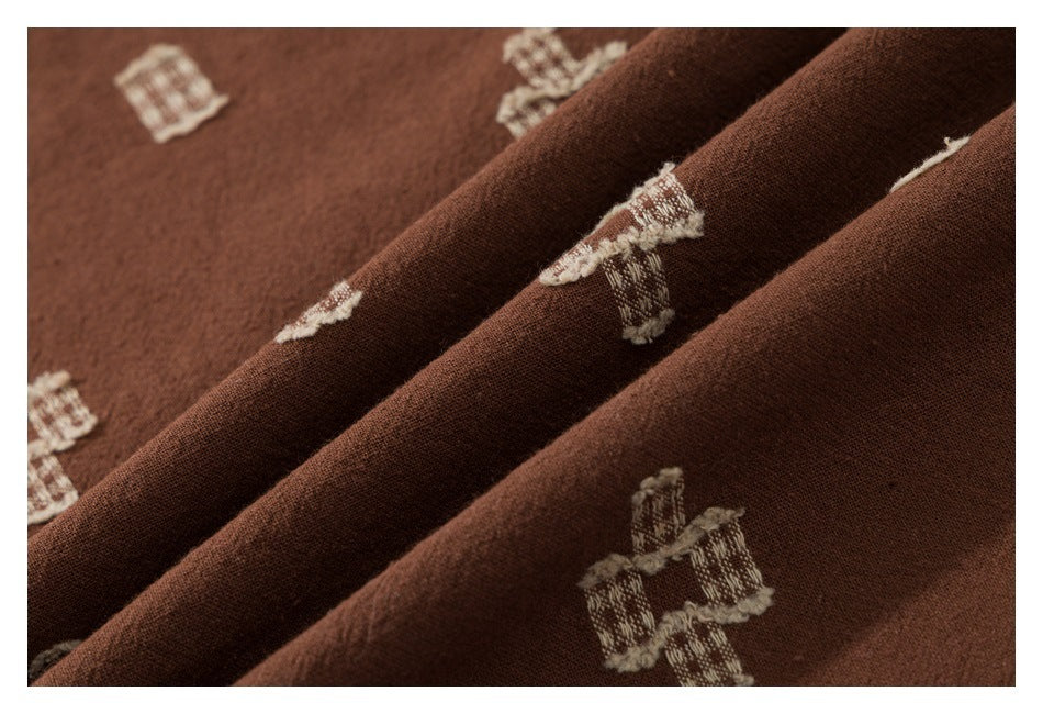 Close-up of brown fabric folds with scattered cream geometric motifs.