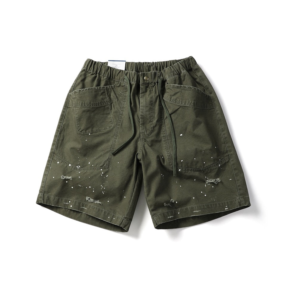 Army green knee-length shorts with elastic drawstring waist, patch pockets, white paint splatters and distressed rips
