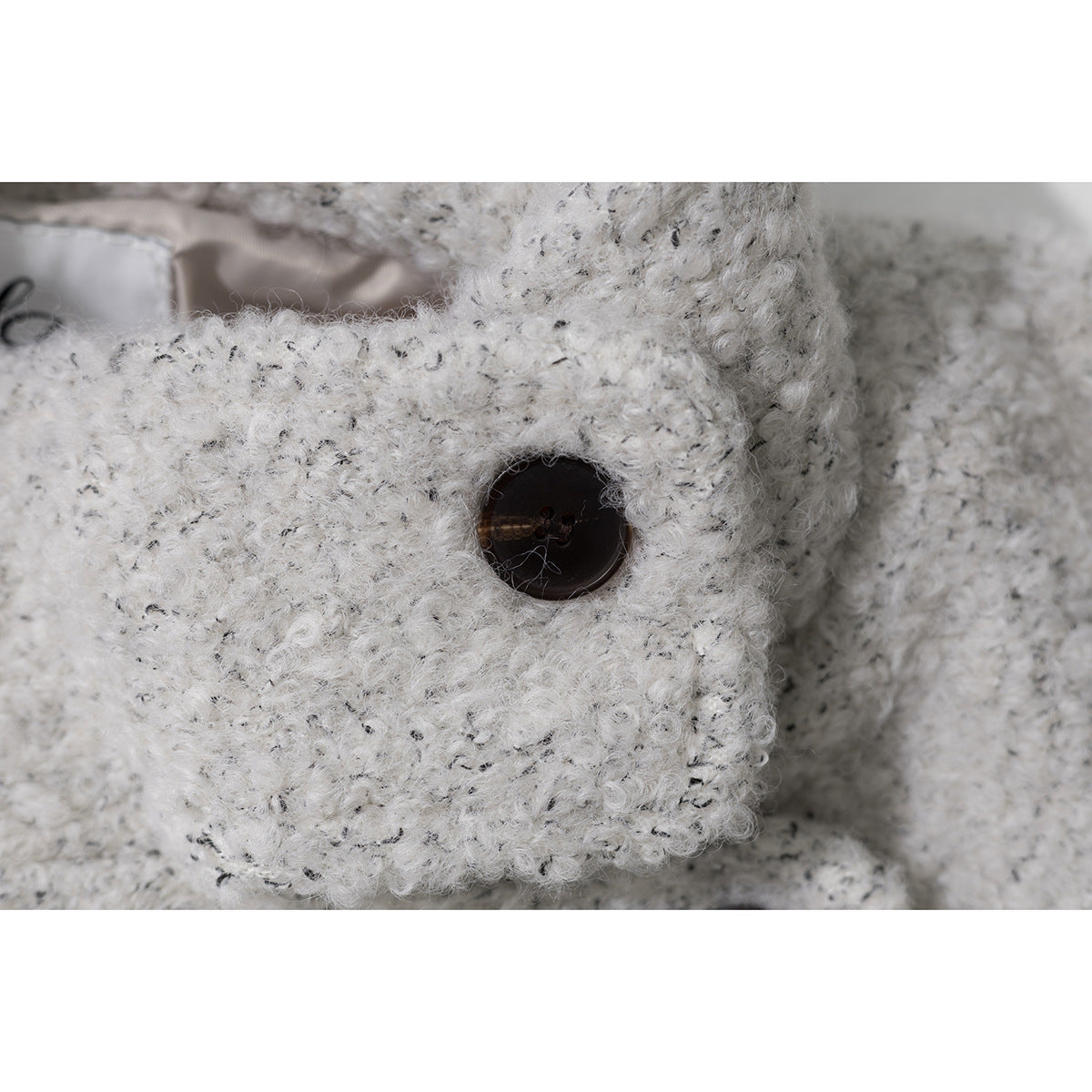 Close-up of an off-white flecked knit garment with a dark button and thick, fuzzy texture.