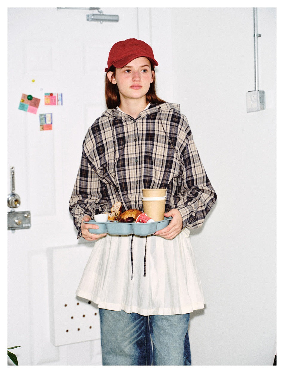 Model wearing a plaid hooded button-up jacket while holding a tray of food and coffee, with white skirt layer and jeans