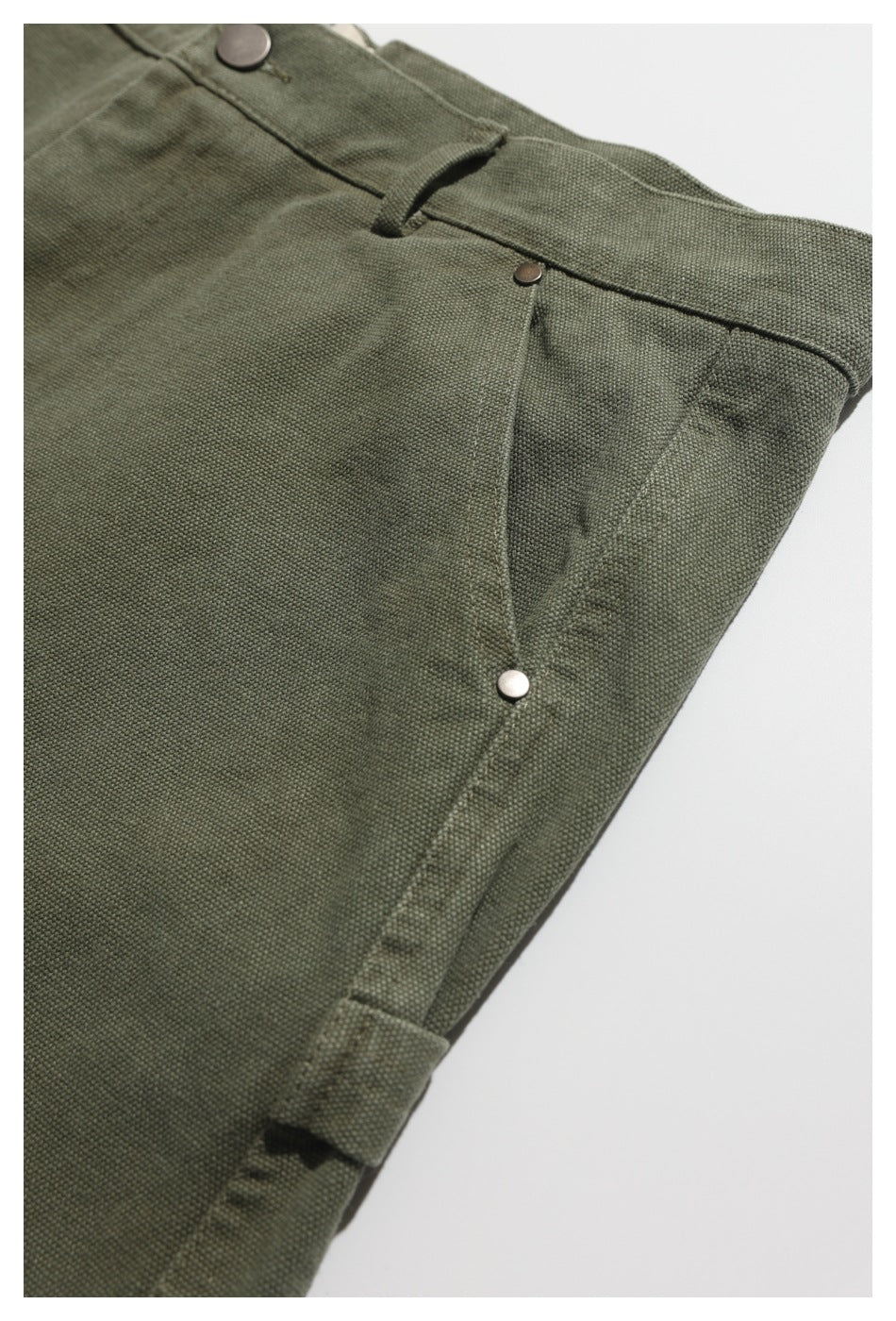 Close-up of olive shorts showing the waistband, button, front pocket rivet, and side seam.