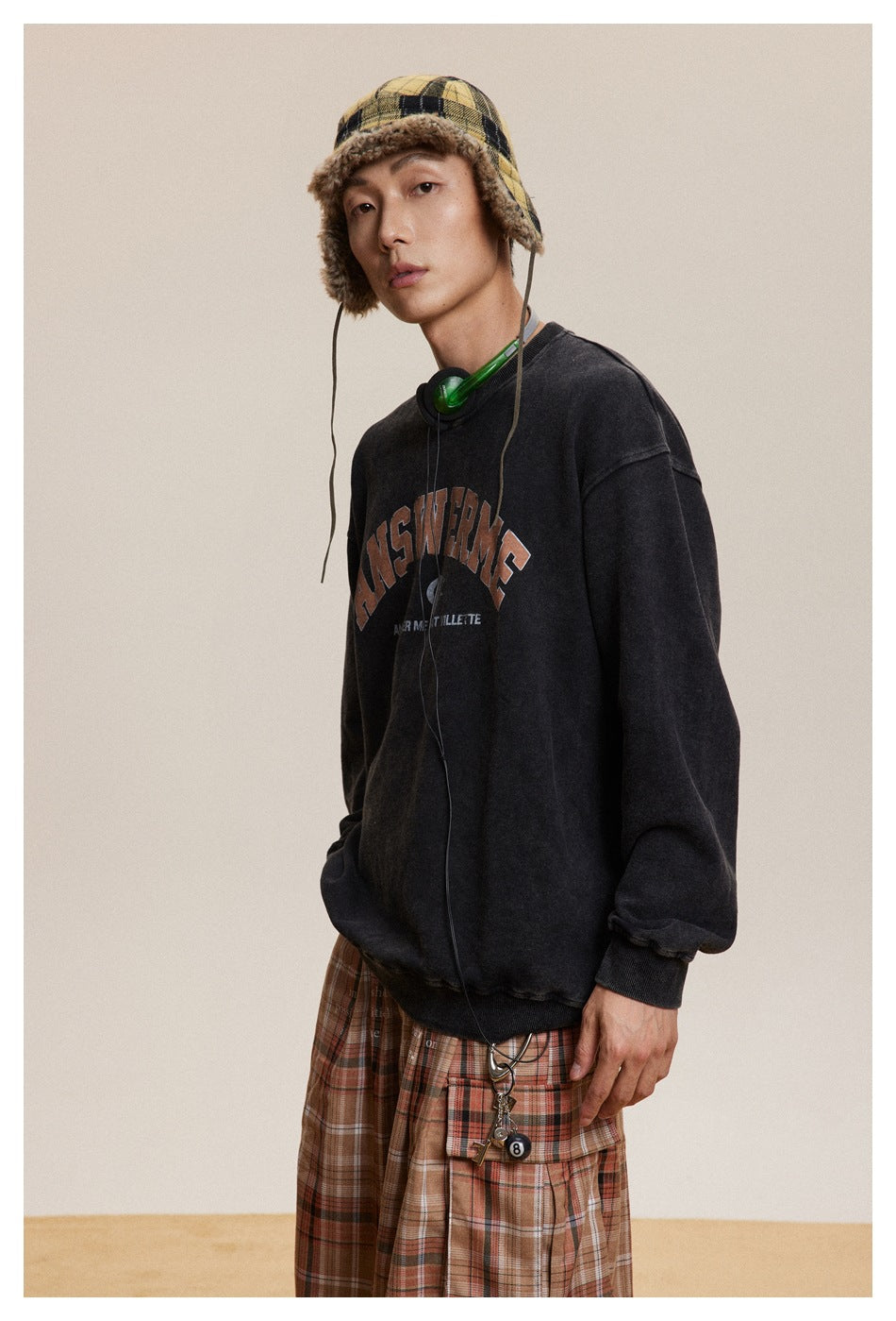 Close view of a model in a washed black graphic sweatshirt and brown plaid cargo trousers.