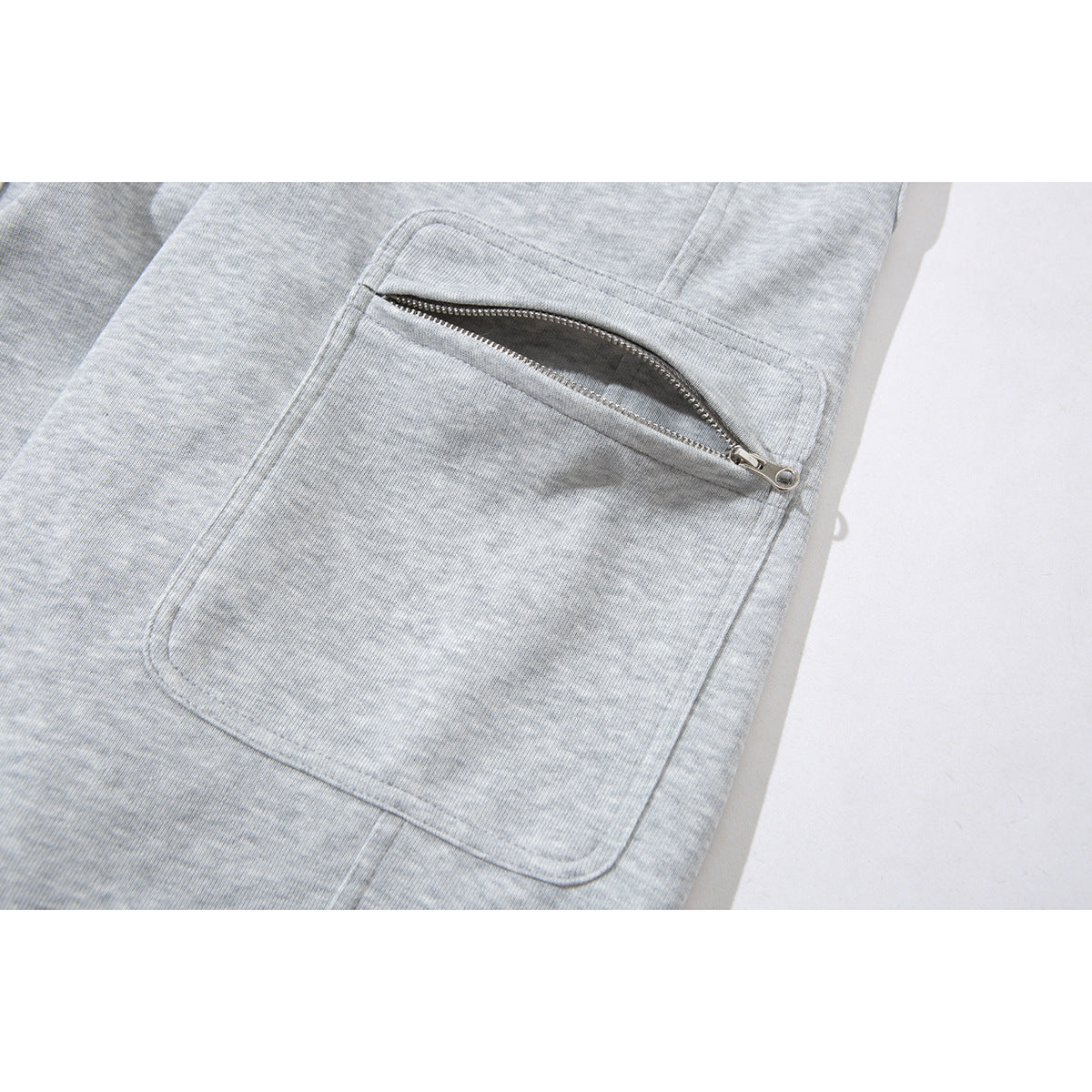 Close-up of a large patch pocket with a silver zipper on light gray sweatpants.