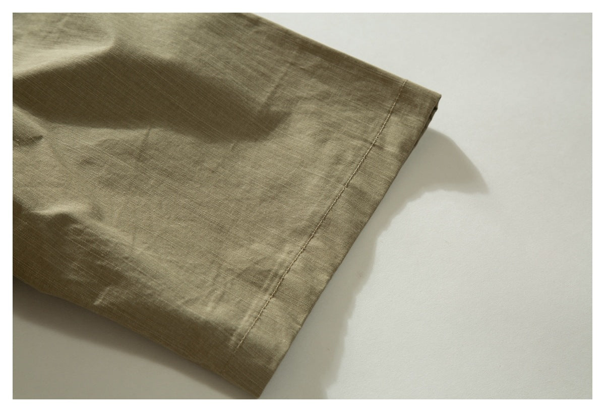 Close-up of the stitched edge of an olive-khaki shirt sleeve lying on a light surface.