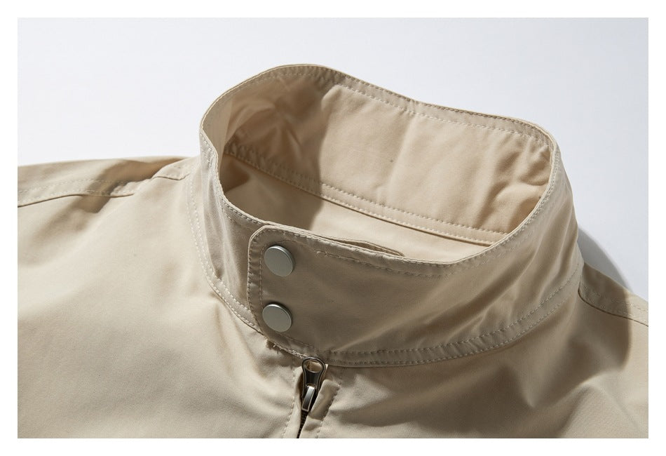Close-up of a beige jacket’s raised stand collar, two metal snaps, and front zipper.