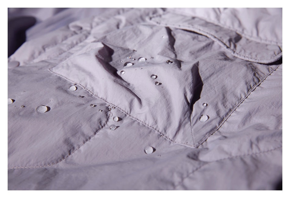 Close-up of a pale lavender garment with water droplets beading on the fabric and pocket flap.