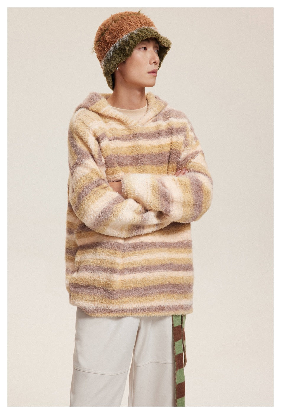 Model in a cream, tan, and mauve striped fuzzy hooded pullover, shown from the front with arms crossed.