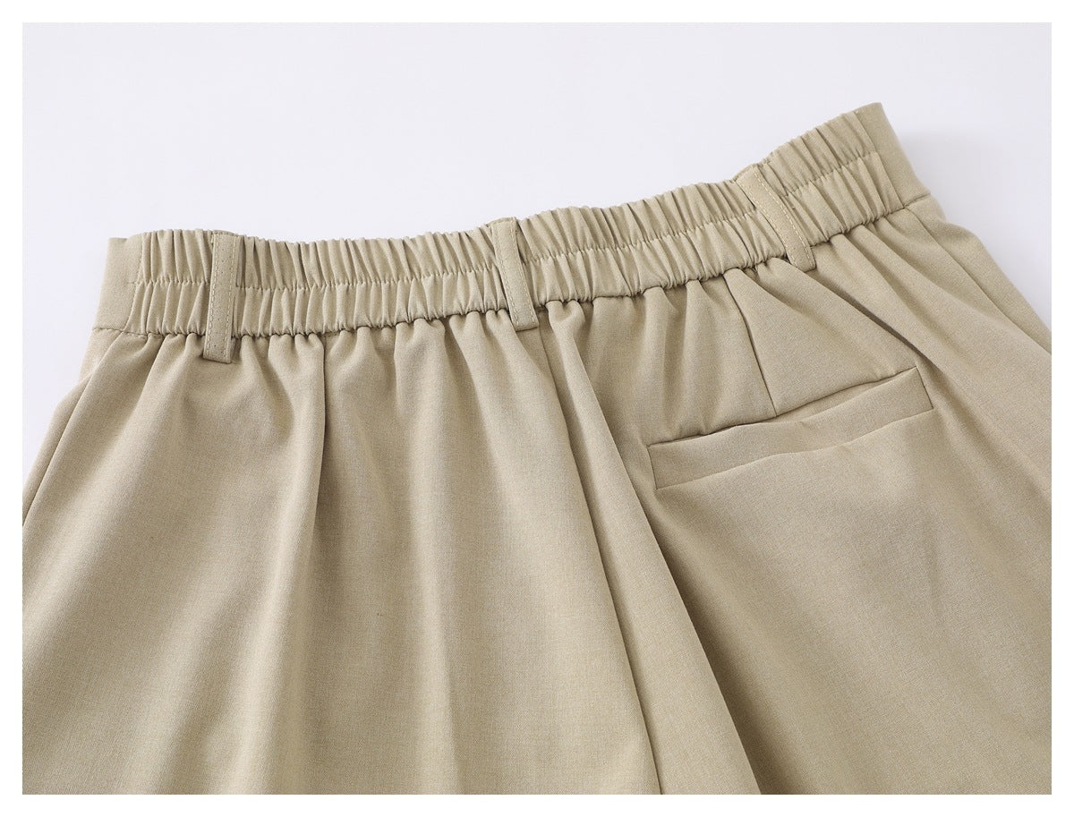 Upper back view of beige trousers with a gathered elastic waistband, belt loops, and welt pocket.