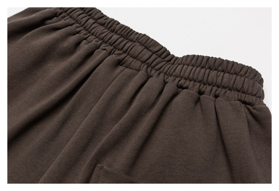 Close-up of dark brown sweatpants showing the gathered elastic waistband and pocket seam.