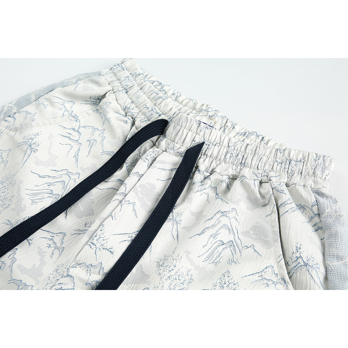 Close-up of white shorts with a pale blue landscape print, elastic waistband, and dark navy drawstrings.