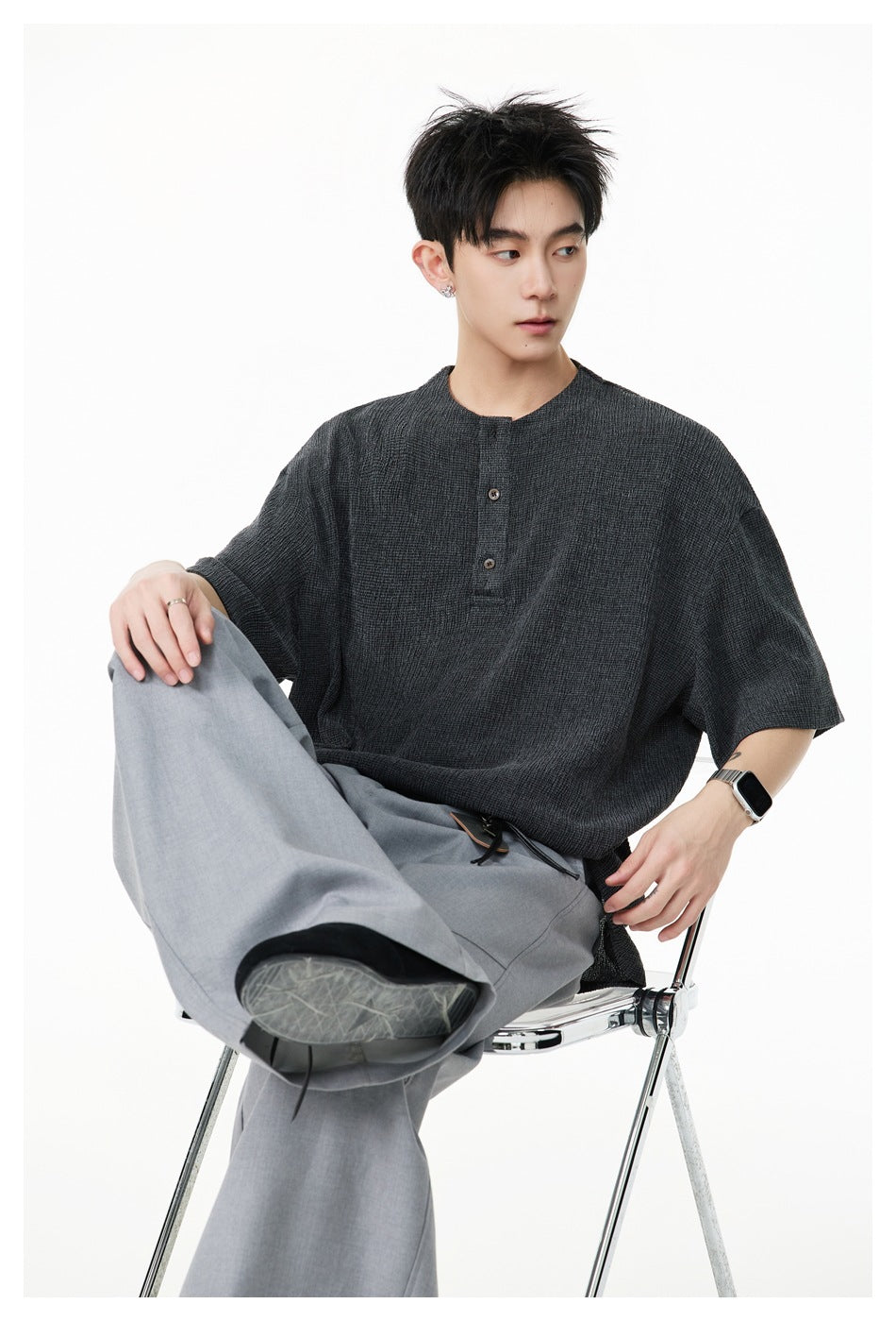 Seated model wearing a charcoal oversized short-sleeve top and gray trousers.