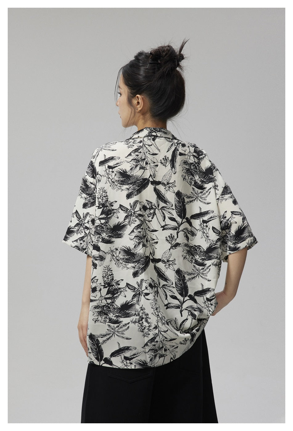 Back view of a model wearing an ivory short-sleeve shirt covered in a black botanical print.
