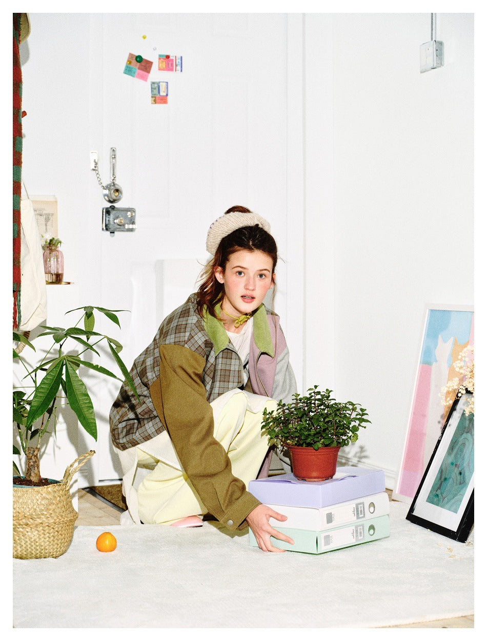 Model crouching in a patchwork jacket with plaid, olive, gray, and dusty pink panels and a green collar.
