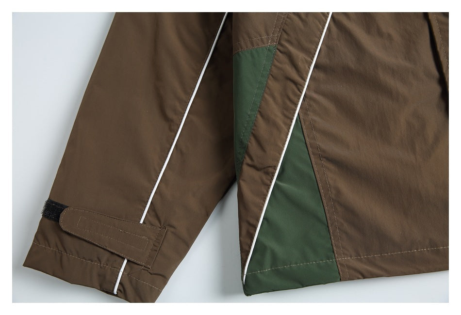 Close-up of a brown jacket with a dark green panel, white piping, and an adjustable sleeve cuff strap.