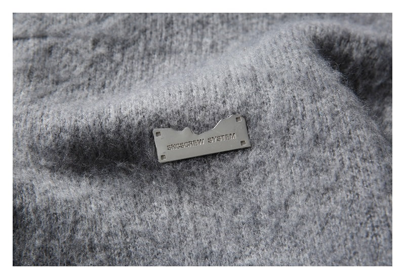 Close-up of a small rectangular metal badge attached to the gray cardigan.