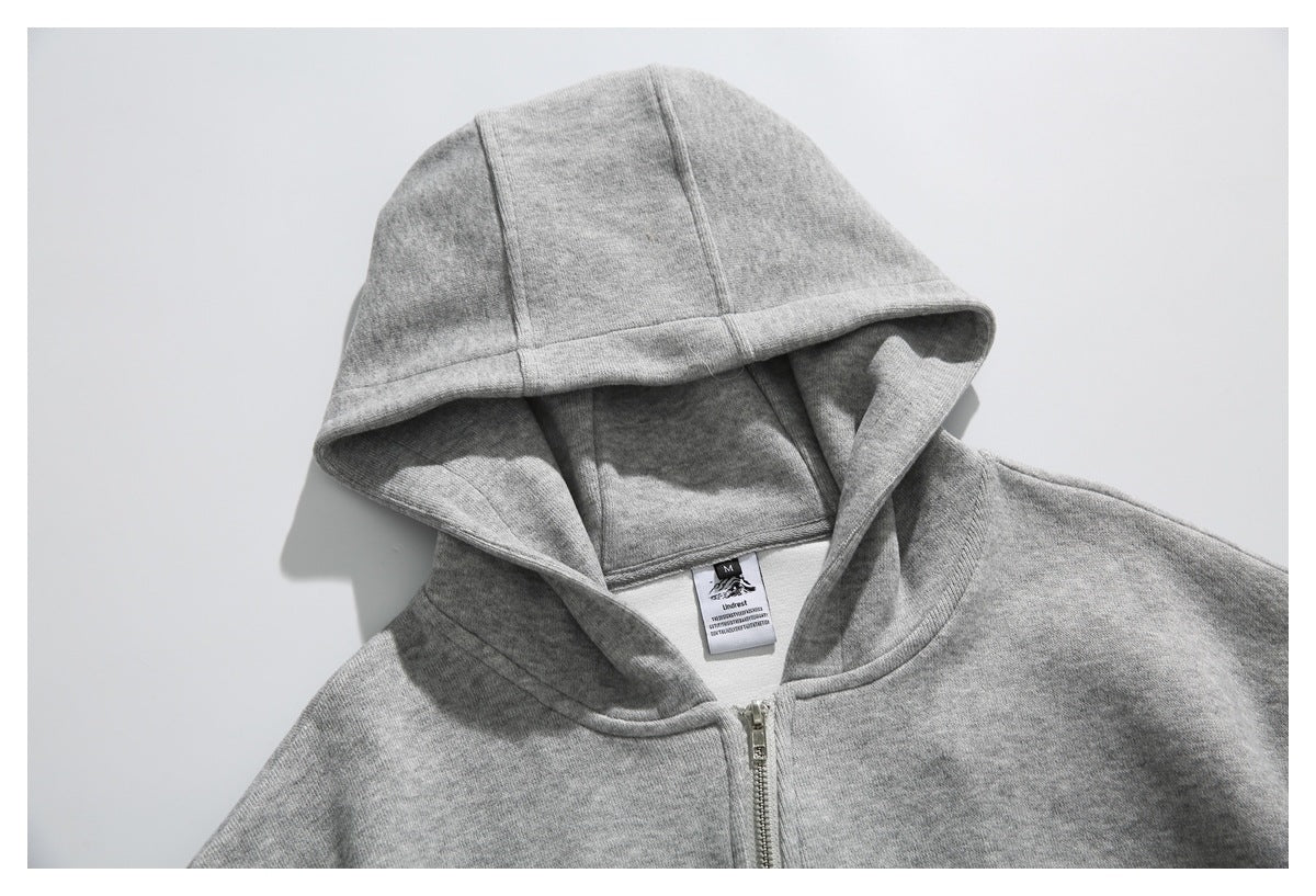 Close-up of a light gray zip-up hoodie showing its hood, zipper, and sewn neck label.