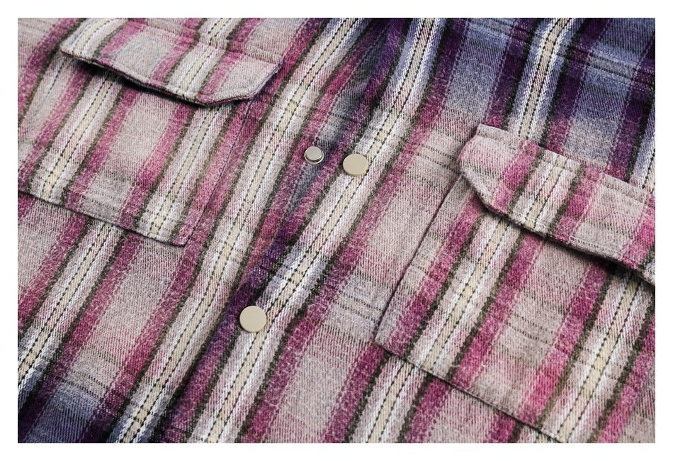 Close-up of a pink, purple, cream, and gray plaid shirt with flap pockets and metal snap buttons.