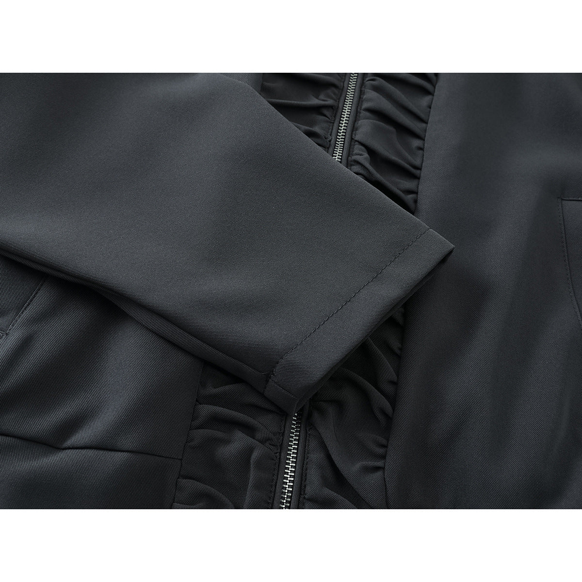 Close-up of a charcoal jacket sleeve crossing the front, with a welt pocket and gathered zipper trim.