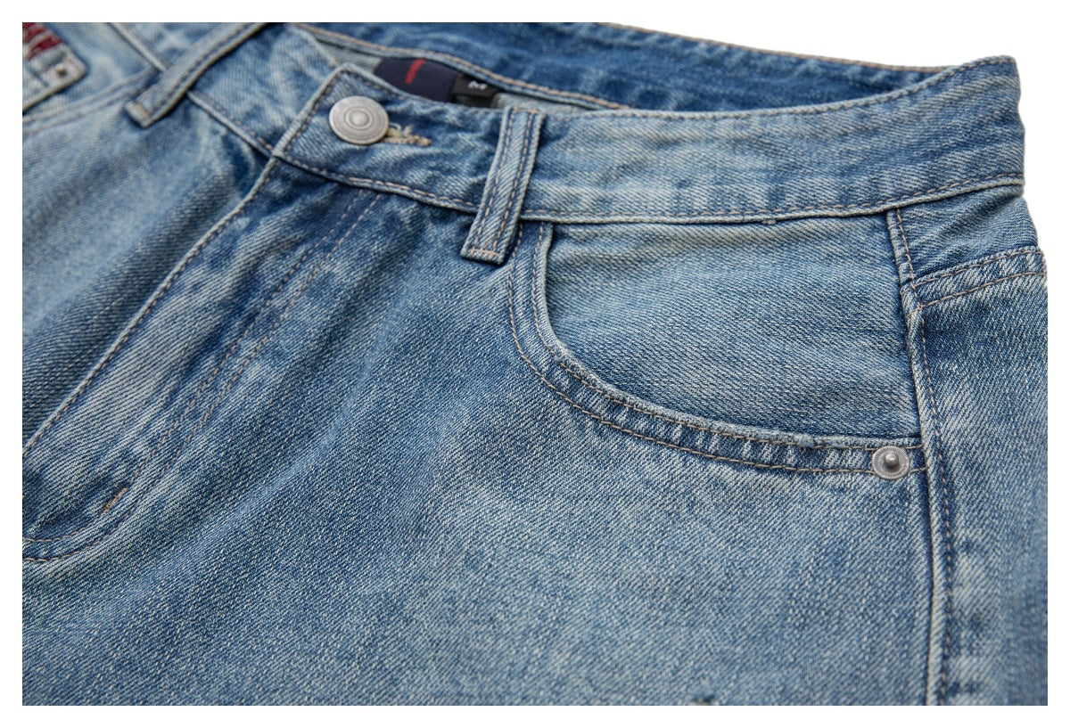 Close-up of blue washed jeans showing the waistband, button, belt loop and curved front pocket.