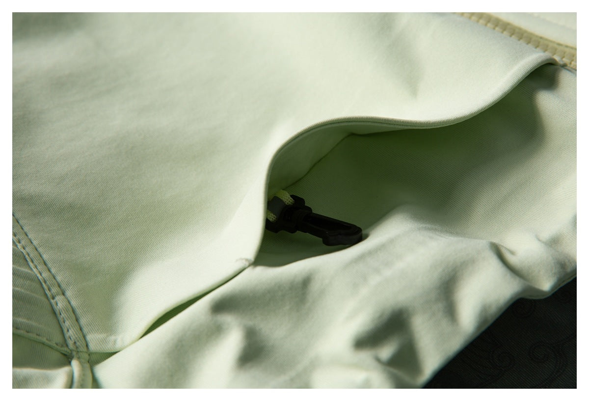 Close-up of pale green jacket fabric and a concealed black toggle beneath a flap.