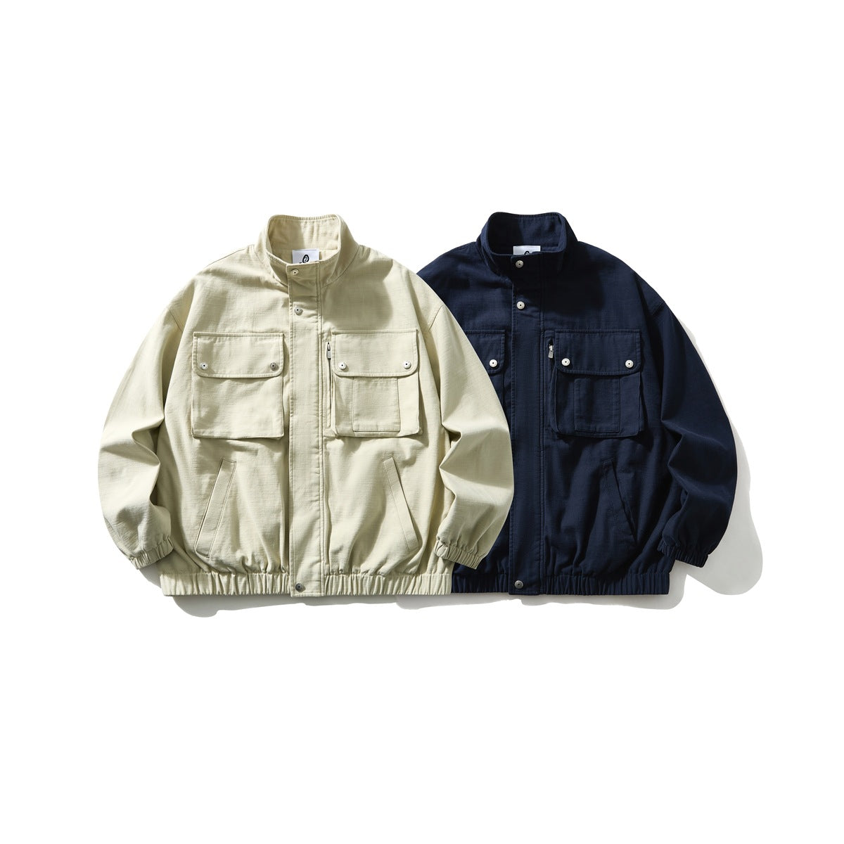 Two front-view utility jackets with stand collars and multiple pockets, in pale beige and navy.