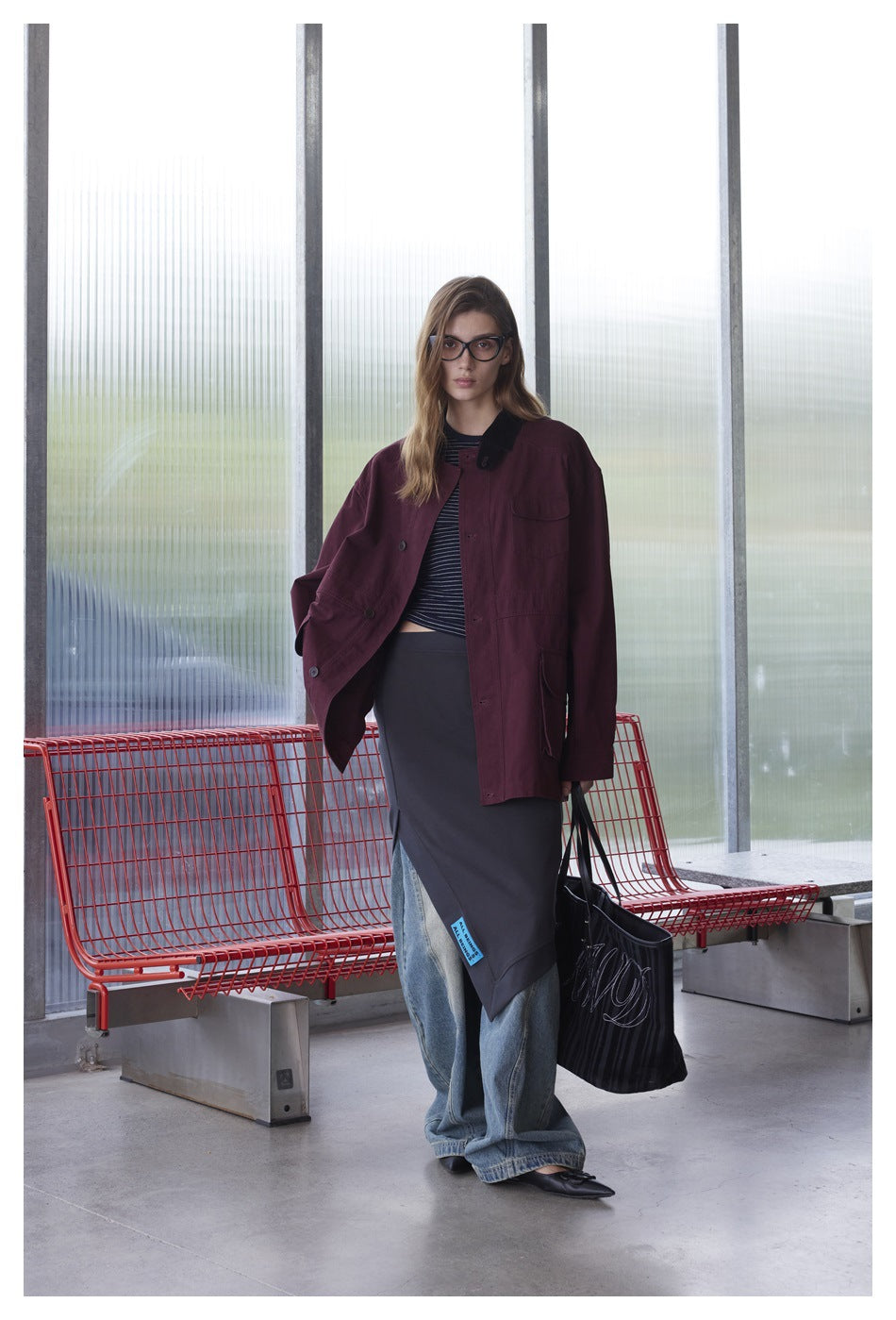 Front view of a model wearing an oversized burgundy jacket with black collar over a striped top and dark skirt.