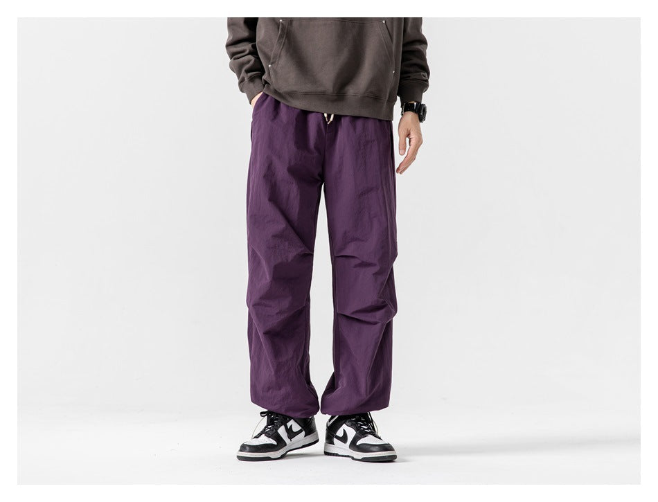 Cropped model wearing loose purple pants in a front view with black-and-white sneakers.