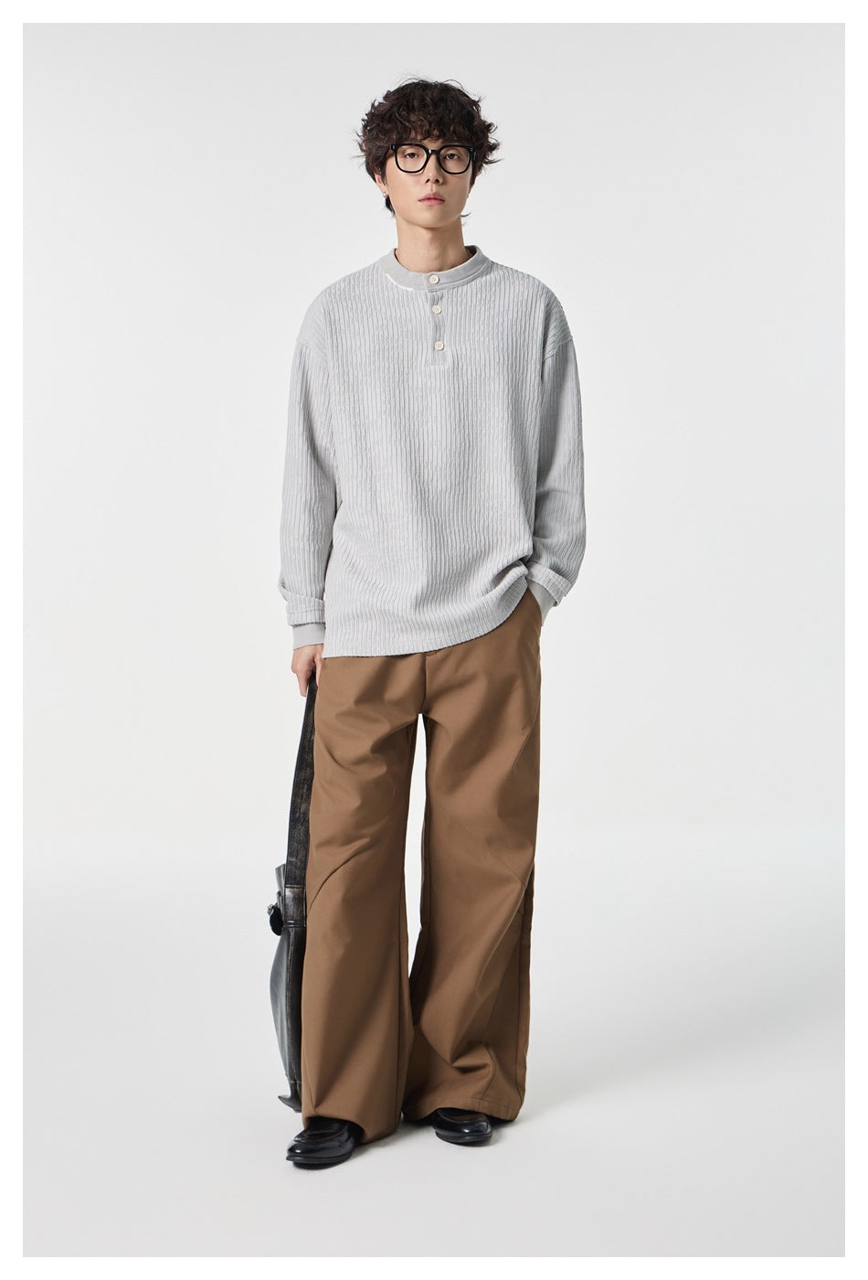 Full-length front view of a model wearing a pale gray textured three-button top and wide brown trousers.