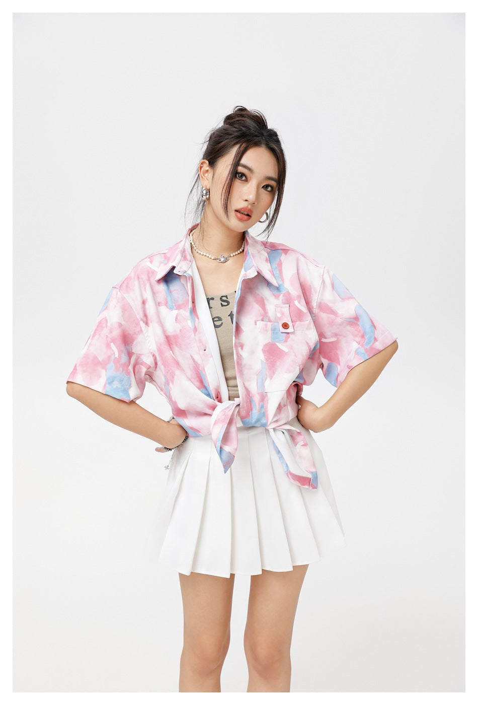 Closer view of a model wearing a pink and blue abstract-print short-sleeve shirt tied over a white pleated skirt.